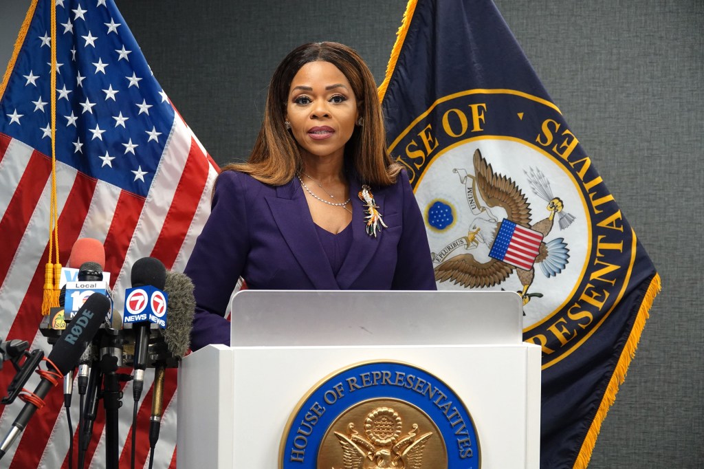 Congresswoman Sheila Cherfilus-McCormick speaks at a news conference, flanked by American and House of Representatives flags.