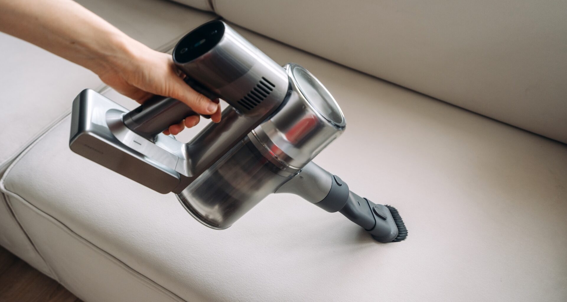 photo showing woman's arm grasping a handheld vacuum cleaner as if cleaning an off-white couch