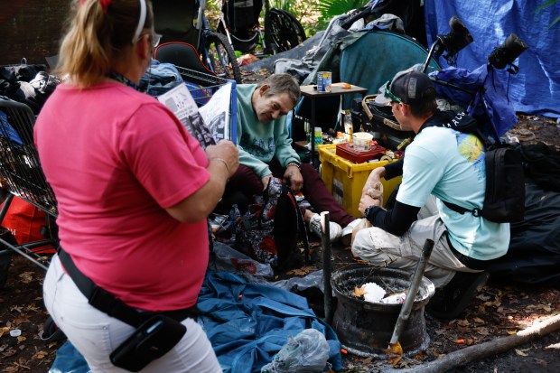 Richie Amabile and Tara Turner from United Global Outreach meet with Gary, a homeless individual who lives in an encampment in a wooded area in Bithlo, on Monday, November 24, 2025. Amabile and Turner are part of a team of peer-support outreach members who go into the woods to check on and try to bring homeless individuals to the mental health treatment programs offered by the organization. (Rich Pope/Orlando Sentinel)
