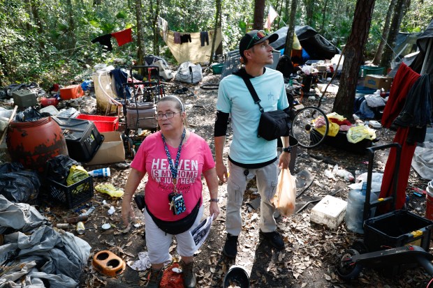 Tara Turner and Richie Amabile look for homeless individuals in an encampment in a wooded area in Bithlo on Monday, November 24, 2025. Amabile and Turner are part of a team of peer support outreach members who go into the woods to check on and try to bring homeless individuals to the mental health treatment programs offered by the organization. (Rich Pope/Orlando Sentinel)