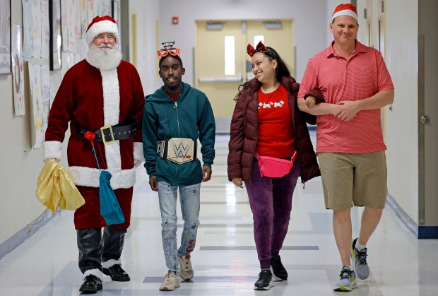 Sun Sentinel staff writer Ben Crandell, dressed as Santa Claus, walks down a hallway at Fort Lauderdale High School with seniors Marquize Young and Maria Jose Alcocer and exceptional student education (ESE) teacher Justin Willard on Monday, Dec. 15, 2025. (Amy Beth Bennett / South Florida Sun Sentinel)