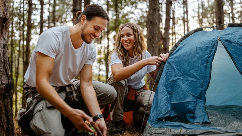 Couple setting up camping tent in forest