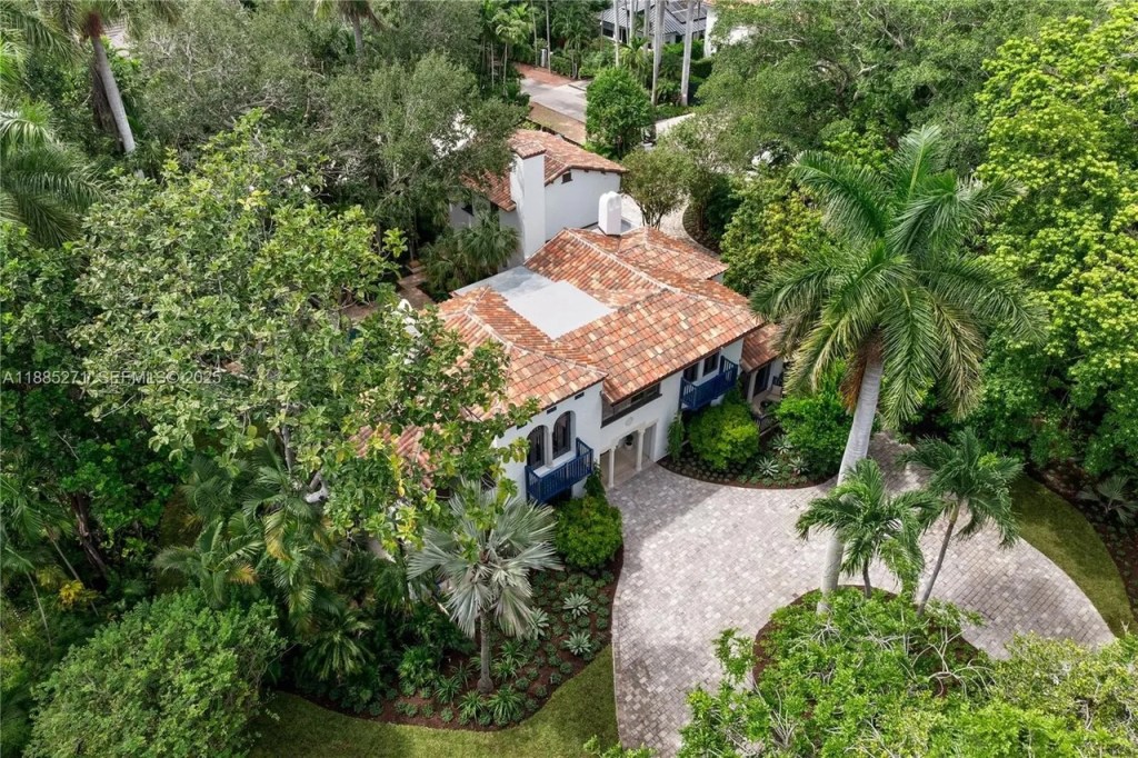 an aerial shot shows a dense thicket of trees and shrubs surrounds a Mediterranean-style home capped with a terra-cotta-colored roof