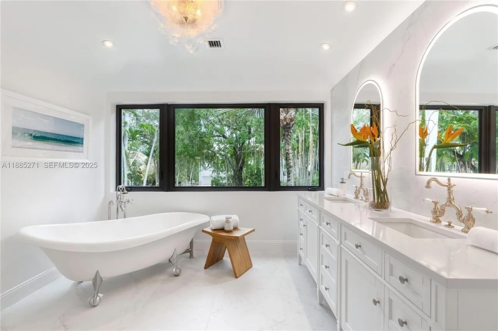 an original-to-home, 100-year-old claw foot tub sits in a stark-white bathroom with a his and her sinks and mirrors
