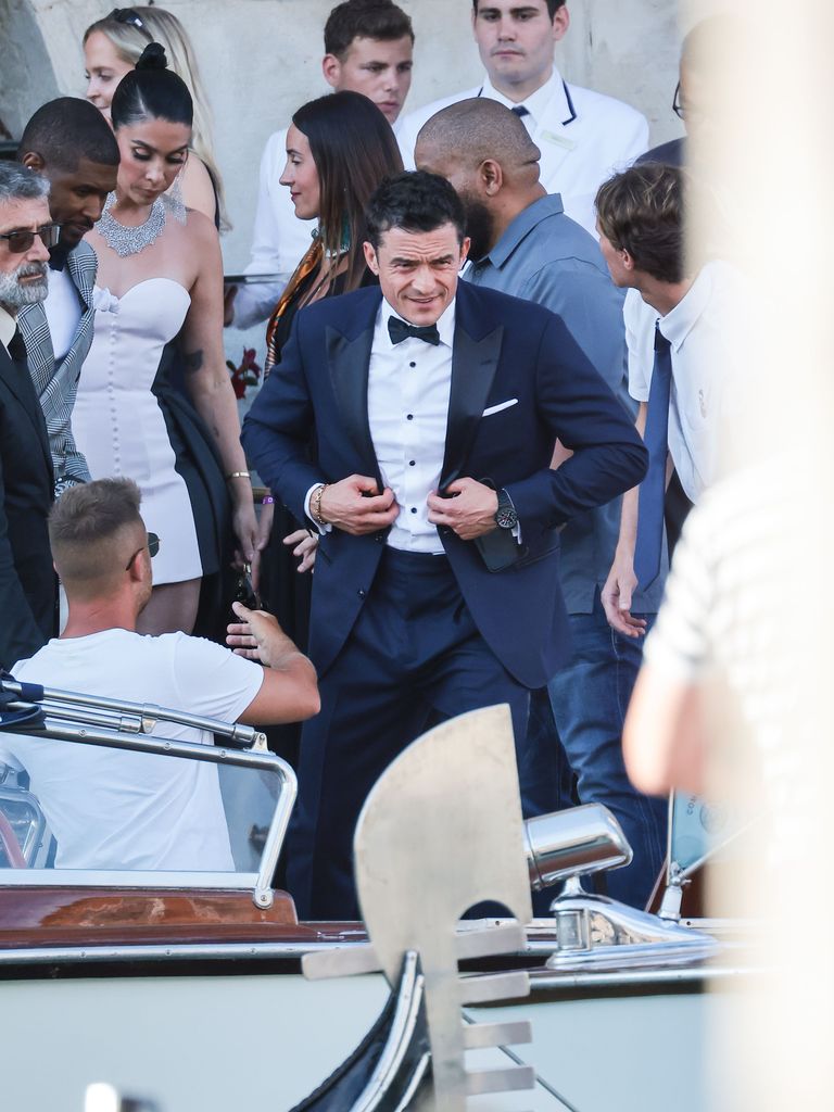 A man wearing a suit and bow tie getting into a boat