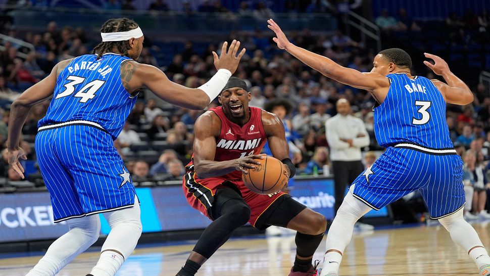 Miami Heat center Bam Adebayo, center, stops short as Orlando Magic center Wendell Carter Jr. (34) and guard Desmond Bane (3) block the path to the basket during the first half of an NBA basketball game, Friday, Dec. 5, 2025, in Orlando, Fla. (AP Photo/John Raoux)