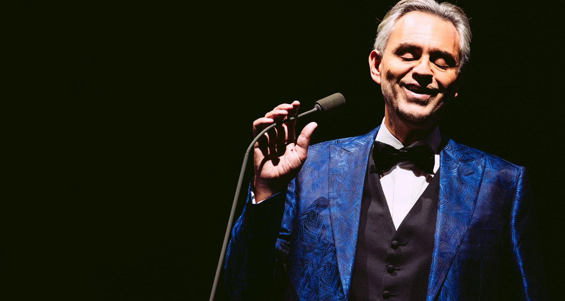 Photo of a man on stage holding a mic wearing a smoking