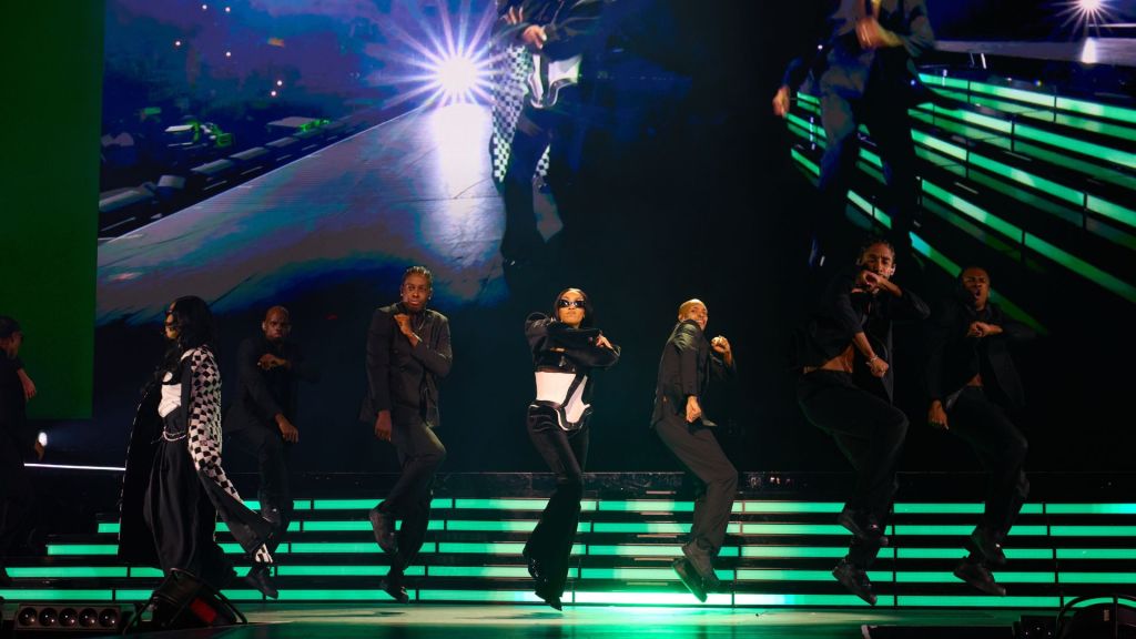 A group of people dancing on stage under green LED lights . 