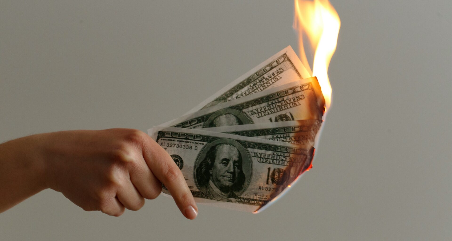 photo of a hand holding four one-hundred-dollar bills on fire