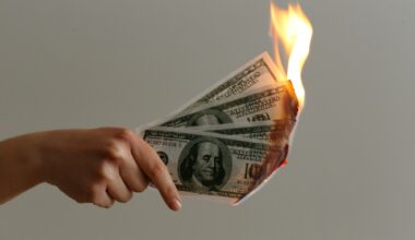 photo of a hand holding four one-hundred-dollar bills on fire