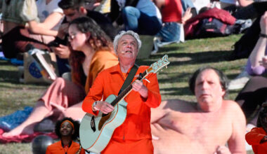 A man wearing an orange jumpsuit on stage playing a guitar.