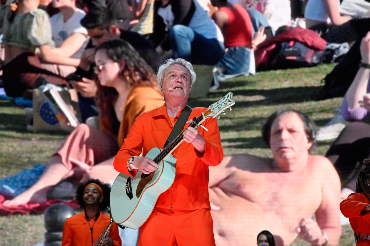 A man wearing an orange jumpsuit on stage playing a guitar.