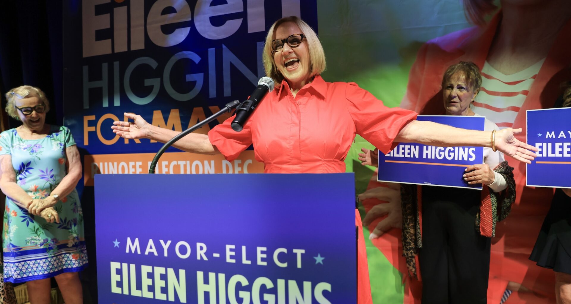 a beaming Eileen Higgins greets supporters from the podium that features a large poster that reads "MAYOR-ELECT EILEEN HIGGINS"