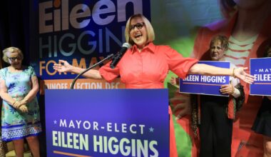 a beaming Eileen Higgins greets supporters from the podium that features a large poster that reads "MAYOR-ELECT EILEEN HIGGINS"