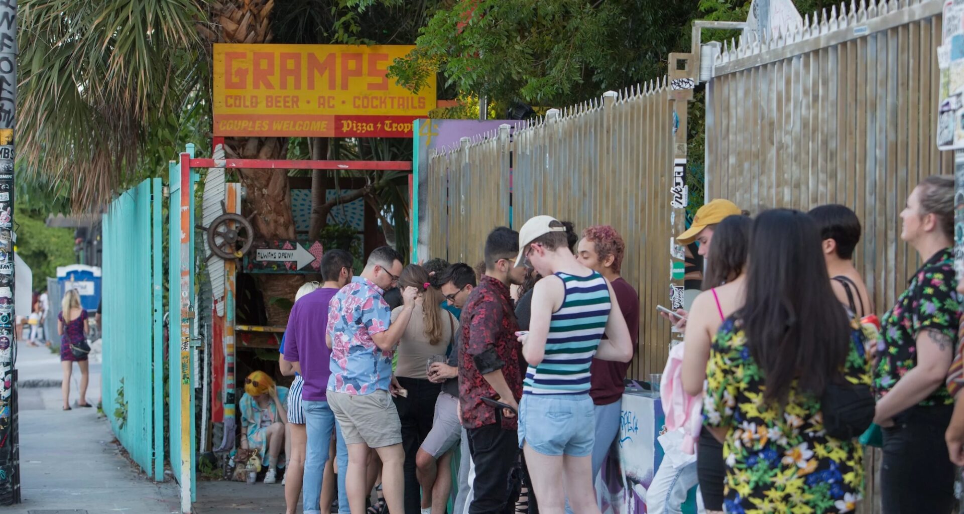 Photo of people in line to enter a bar. A painted wooden sign at the venue reads, "Gramps"