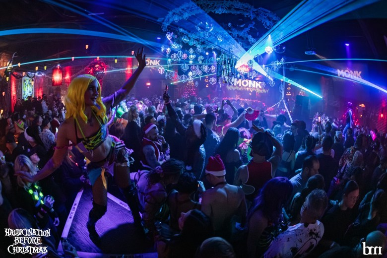 https://www.cltampa.com/music-2/tampa-bays-best-live-music-happening-december-11-18/A large group of people celebrating at a club. A performer in the foreground, wearing a yellow wig and a brightly colored outfit, strikes a dramatic pose with a hand raised on a platform overlooking the crowd.