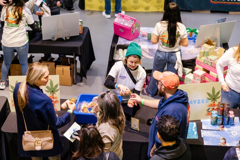 A vendor in a teal beanie pours a sample of a Dayzed beverage for an attendee at a crowded booth during the High & Dry Festival.