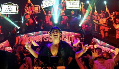 photo of DJ John Summit performing at a club with bottle girls holding up signs behind him