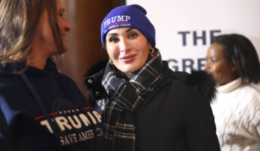 Laura Loomer wears a blue beanie looking at the camera with a closed-mouth smile. She is wearing a black scarf and a puffer coat with a fur hood.