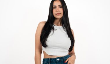 photo of a woman with long black hair in a white crop top and jeans posing in front of a white backdrop