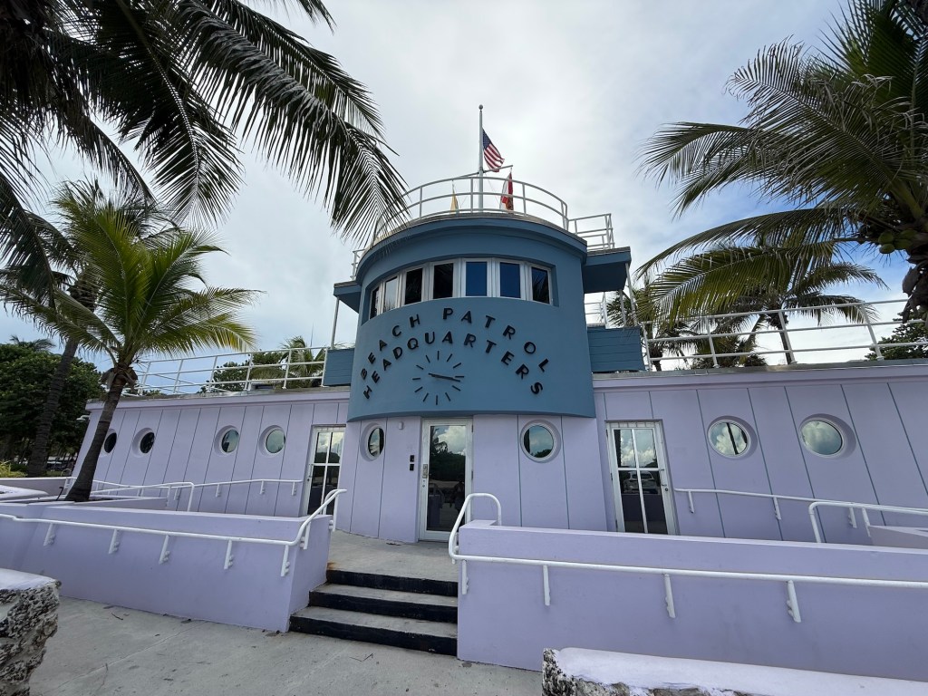 photo of an Art Deco-style building painted blue and lilac, with a sign reading, "Beach Patrol Headquarters"