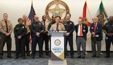 Miami-Dade Sheriff Rosie Cordero-Stutz speaks at a podium wearing her police uniform surrounded by Miami-Dade Sheriff's Office police officers and officers from the Miami Police Department.