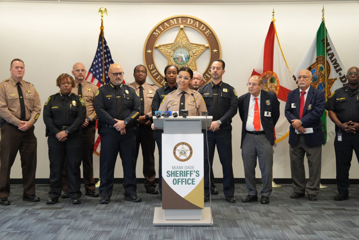 Miami-Dade Sheriff Rosie Cordero-Stutz speaks at a podium wearing her police uniform surrounded by Miami-Dade Sheriff's Office police officers and officers from the Miami Police Department.