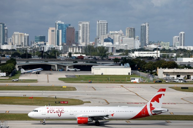 With a view of downtown Fort Lauderdale, an Air Canada plane taxis to the end of the runway for takeoff at Fort Lauderdale/Hollywood International Airport is loaded onto a tow truck on Thursday, Dec. 18, 2025. (Amy Beth Bennett / South Florida Sun Sentinel)