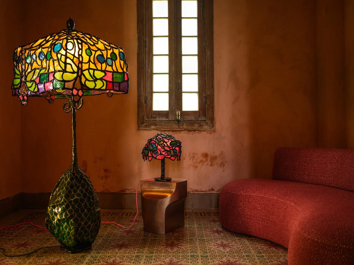 Room with large and small stained glass lamps, red sofa, decorative floor, and window with grid design.