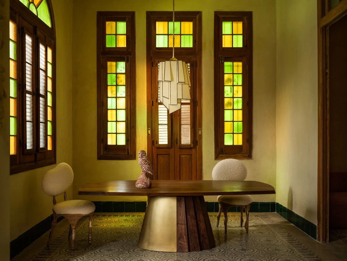 Elegant room with stained glass windows, modern wooden table, decorative sculpture, and two stylish chairs.