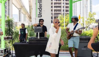 Photo of a bald woman on stage holding a microphone at an outdoors venue.