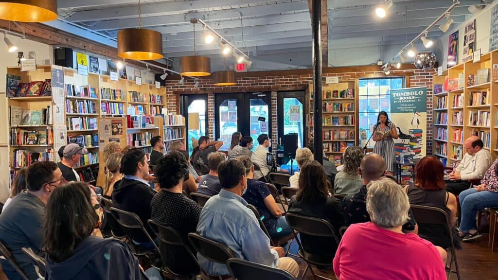 a group of people watch a poet on stage inside of a bookstore