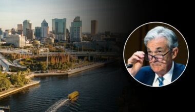 A view of downtown Tampa along the river with an inset photo of Federal Reserve Chair Jerome Powell adjusting his glasses.
