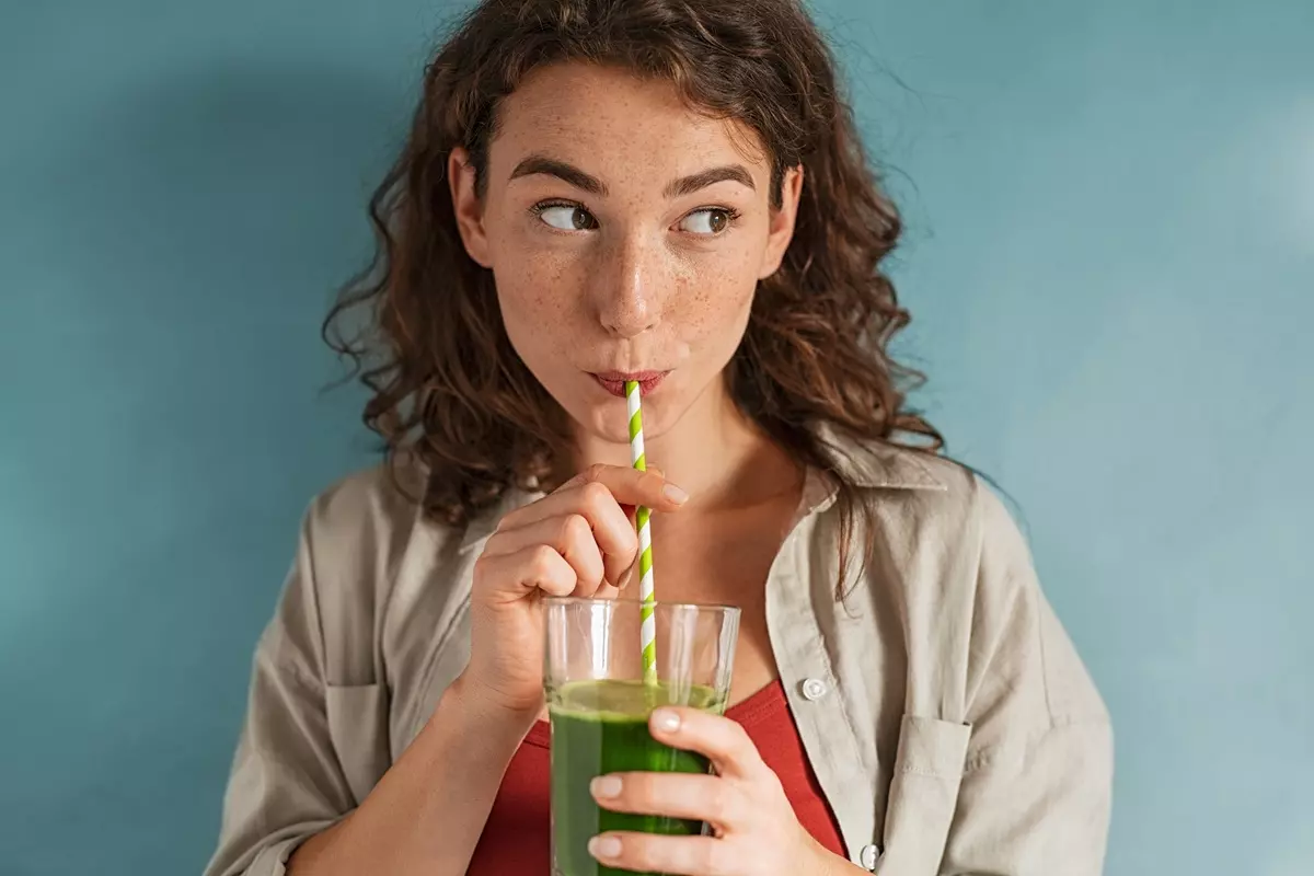 A young woman drinking a detox juice with a straw.