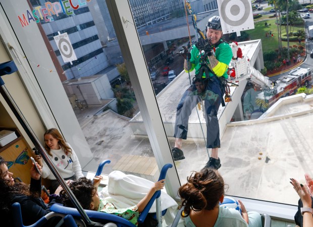 Orange County Fire Rescue Battalion Chief Thomas Farrel waves to Kaleb Muniz and Elijah Brown, patients at AdventHealth for Children, as Orange County Fire Rescue and the Orlando Fire Department rappel down the side of the building, interacting with children and their families through the windows. Now in its ninth year, the "Elf Rappel" event has become a tradition for Orlando-area fire departments. Dressed as elves, they spread cheer down the side of the children hospital with help from Santa and Mrs. Claus, who are also high above on ladder trucks, playing along in their usual jolly manner.(Rich Pope/Orlando Sentinel)