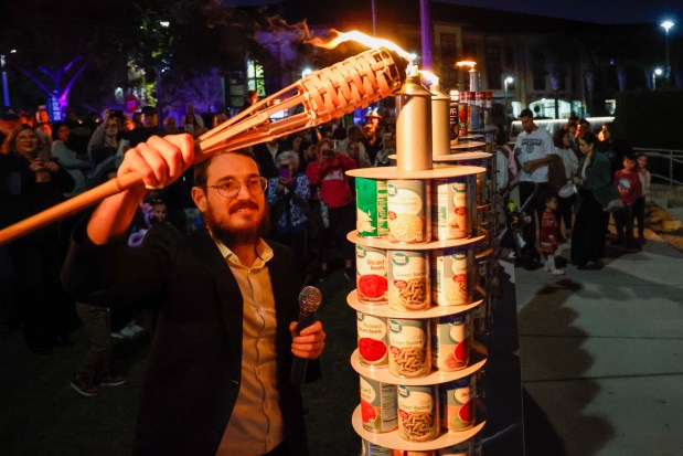 Rabbi Tzvi Dubov, of Chabad of Oviedo-Winter Springs, lights the two candles on the menorah created out of canned goods that will be donated to the Second Harvest Food Bank of Central Florida during a Hanukkah celebration at Center Lake Park in Oviedo on Monday, December 15, 2025. (Rich Pope/Orlando Sentinel)