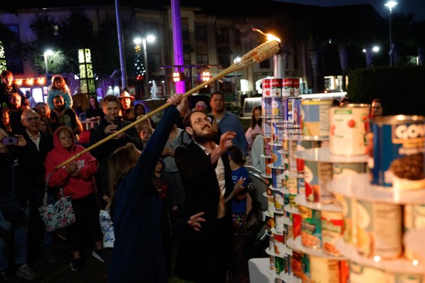 Rabbi Tzvi Dubov, of Chabad of Oviedo-Winter Springs, gets some help lighting the shamash, the "helper" candle, before the lighting of the two candles on the menorah on the second night of Hanukkah during a celebration at Center Lake Park in Oviedo on Monday, December 15, 2025. (Rich Pope/Orlando Sentinel)