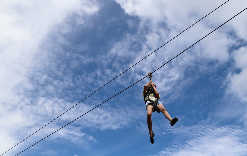 Stock photo of a boy gliding on an extreme trolley zip line in adventure park with scattered clouds in the background on a sunny day.