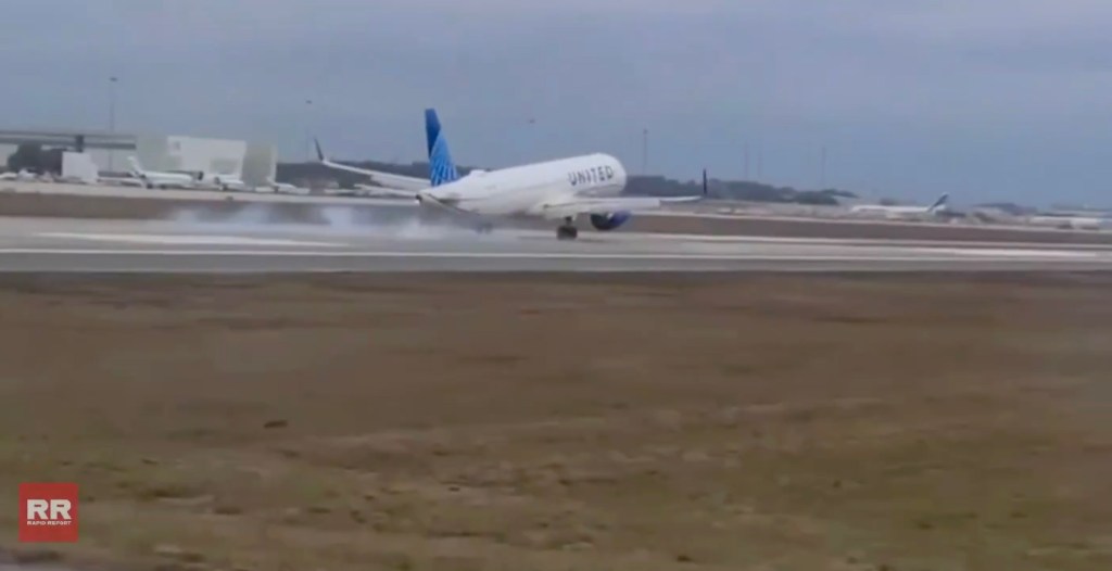 A United airplane lands on a wet runway, kicking up spray.