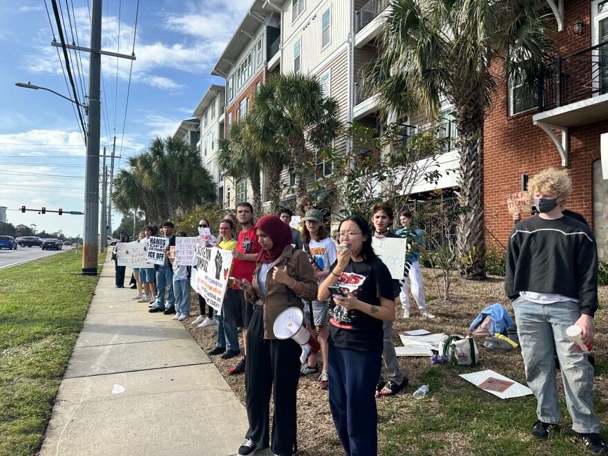 protestors stand along a sidewalk outside of USF campus