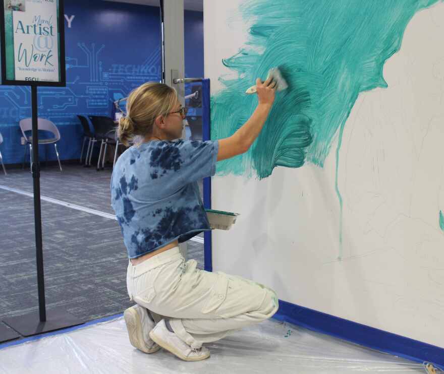 Muralist Macy Noll splashes color on wall adjacent to library's Information Desk.