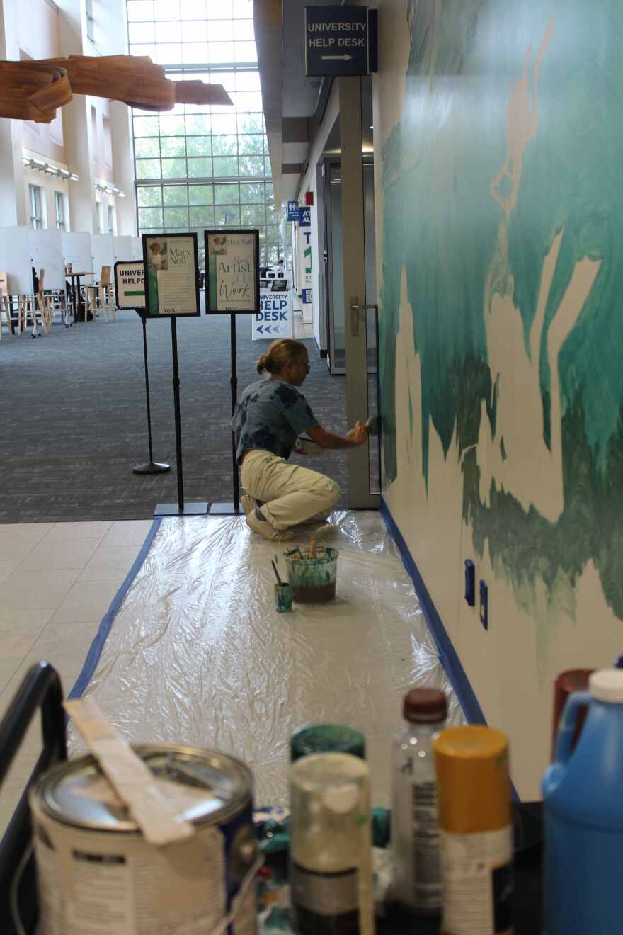 Muralist Macy Noll at work inside the Wilson G. Bradshaw Library at FGCU.