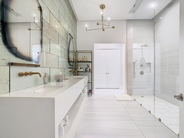 The primary bathroom has a gigantic, walk-in shower with multiple rainhead faucets. The opposite wall features an oversized vanity and designer glass tile. (Photo by Tyto Media)
