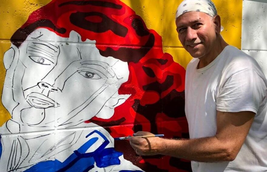 Muralist Roland Ruocco working on panel of the Buck's Backyard mural at McCollum Hall.