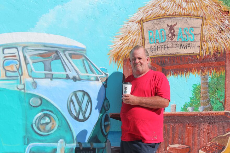 Muralist Erik Schlake posing with mural he recently painted for Bad Ass Coffee on Fort Myers Beach.