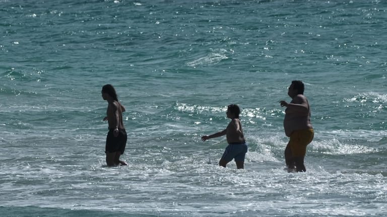 Beachgoers brave the cold ocean temperature while walking on a...