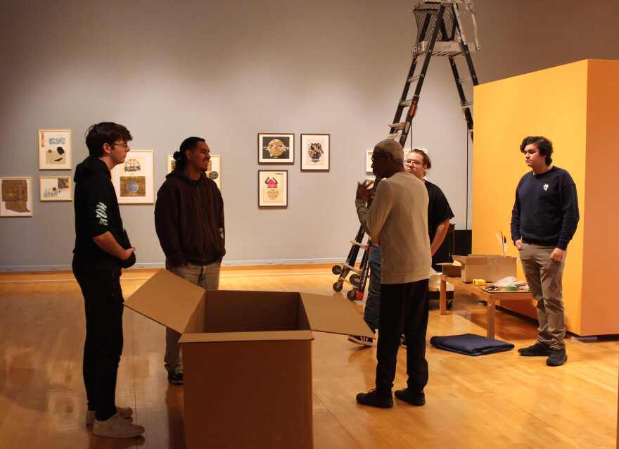 Artist Onajide Shabaka (white shirt, back turned) discusses art and process with members of the FGCU Jazz Combo.