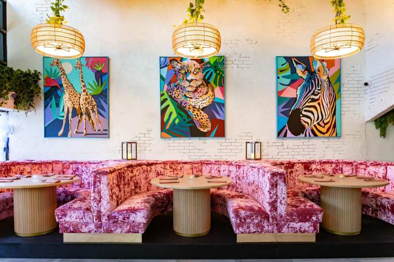 Trendy dining space with crushed velvet pink seating, rattan lighting, and pop-art style animal portraits.