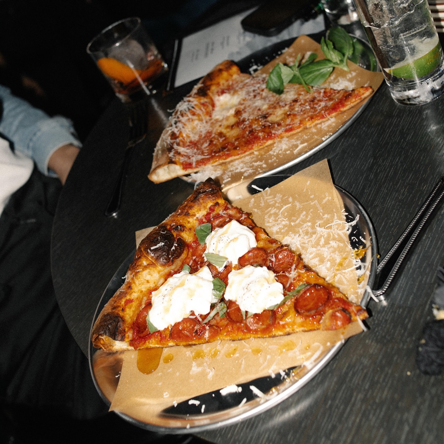 Plates of pizza slices and a cocktail on a table.