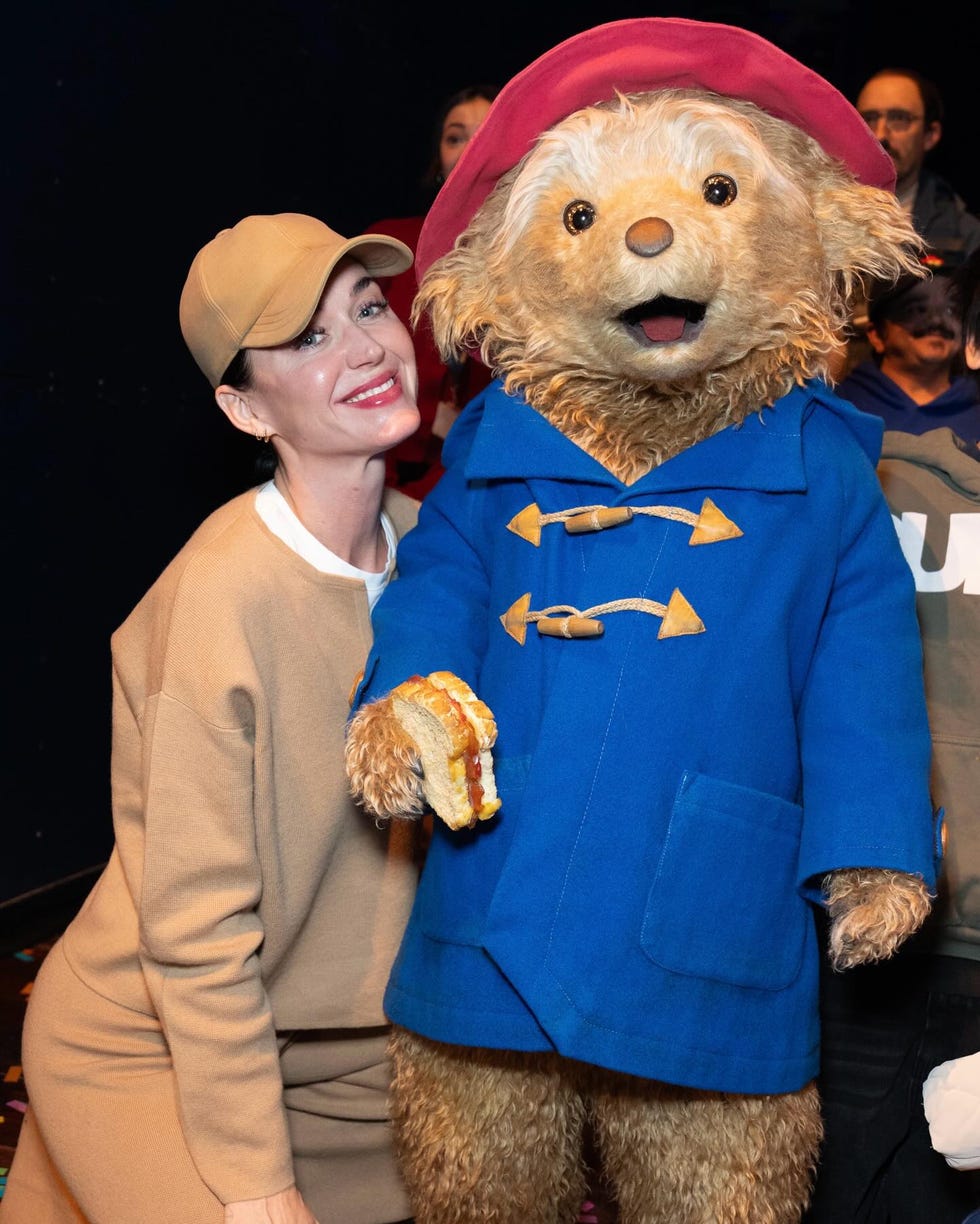 person posing with a bear character in a blue coat holding a sandwich